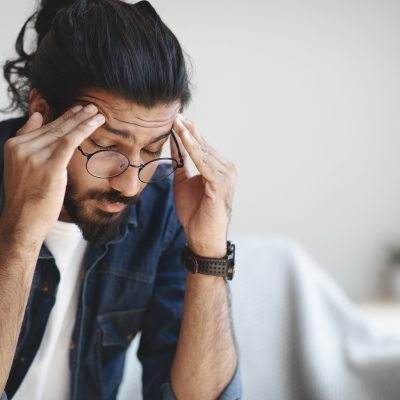 Young indian guy freelancer suffering from headache after hard working day